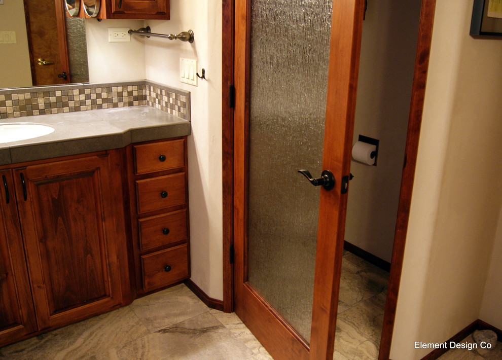 Klassisk inredning av ett badrum, med ett undermonterad handfat, luckor med upphöjd panel, skåp i mörkt trä, kaklad bänkskiva, ett fristående badkar, en hörndusch, en toalettstol med separat cisternkåpa, grå kakel och porslinskakel