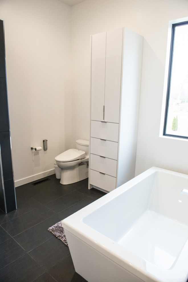 Exempel på ett stort modernt vit vitt badrum, med släta luckor, vita skåp, ett fristående badkar, en öppen dusch, en bidé, grå kakel, porslinskakel, vita väggar, klinkergolv i keramik, ett avlångt handfat, bänkskiva i kvarts, grått golv och med dusch som är öppen
