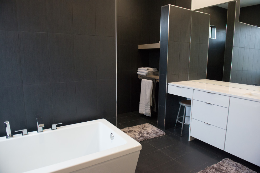 Modern inredning av ett stort vit vitt badrum, med släta luckor, vita skåp, ett fristående badkar, en öppen dusch, en bidé, grå kakel, porslinskakel, vita väggar, klinkergolv i keramik, ett avlångt handfat, bänkskiva i kvarts, grått golv och med dusch som är öppen