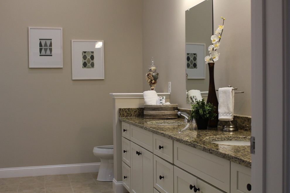 Cette image montre une grande salle de bain traditionnelle avec un placard à porte affleurante, des portes de placard blanches, WC séparés, un carrelage beige, des carreaux de porcelaine, un mur beige, un sol en carrelage de porcelaine, un lavabo encastré et un plan de toilette en granite.