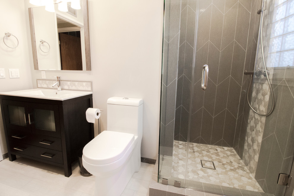 Bild på ett litet funkis badrum med dusch, med släta luckor, skåp i mörkt trä, en hörndusch, en toalettstol med hel cisternkåpa, grå kakel, keramikplattor, grå väggar, klinkergolv i keramik, ett integrerad handfat och bänkskiva i akrylsten