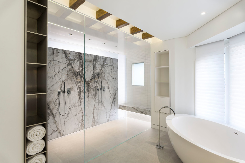 Пример оригинального дизайна: большая главная ванная комната в стиле модернизм с плоскими фасадами, белыми фасадами, отдельно стоящей ванной, открытым душем, серой плиткой, стеклянной плиткой, белыми стенами, полом из известняка, монолитной раковиной, мраморной столешницей, серым полом и открытым душем