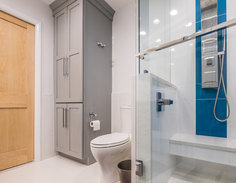This is an example of a medium sized modern ensuite bathroom in Detroit with flat-panel cabinets, grey cabinets, an alcove shower, a one-piece toilet, blue tiles, glass tiles, white walls, a submerged sink, quartz worktops, white floors and a hinged door.