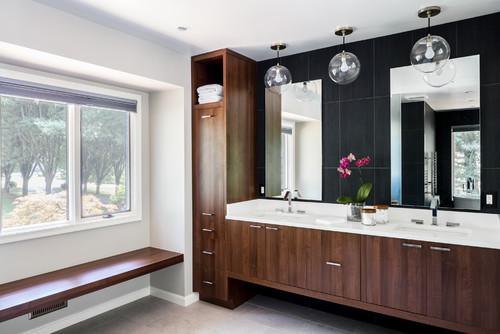 Contemporary bathroom with dark wood floating bathroom cabinets, white countertop, double sinks, tall storage tower, and black accent wall with large mirrors.