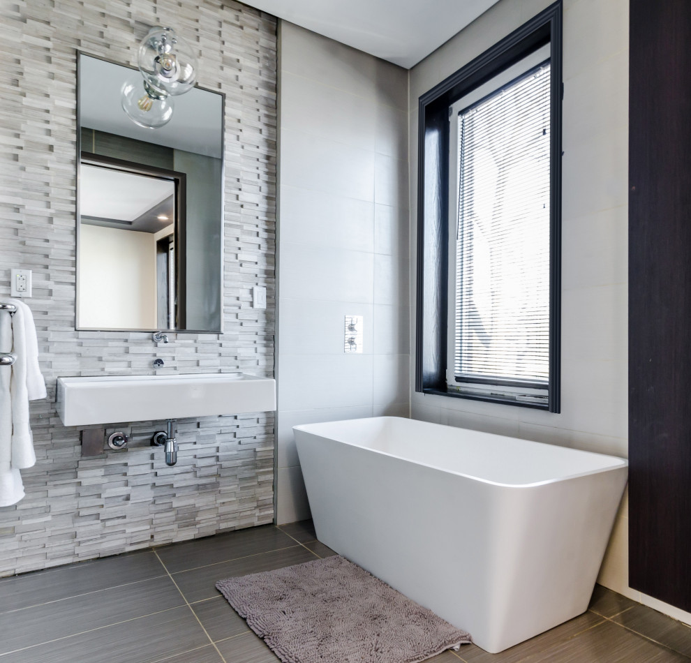 Стильный дизайн: главная ванная комната среднего размера в стиле модернизм с отдельно стоящей ванной, белыми стенами, полом из керамической плитки, подвесной раковиной и серым полом - последний тренд