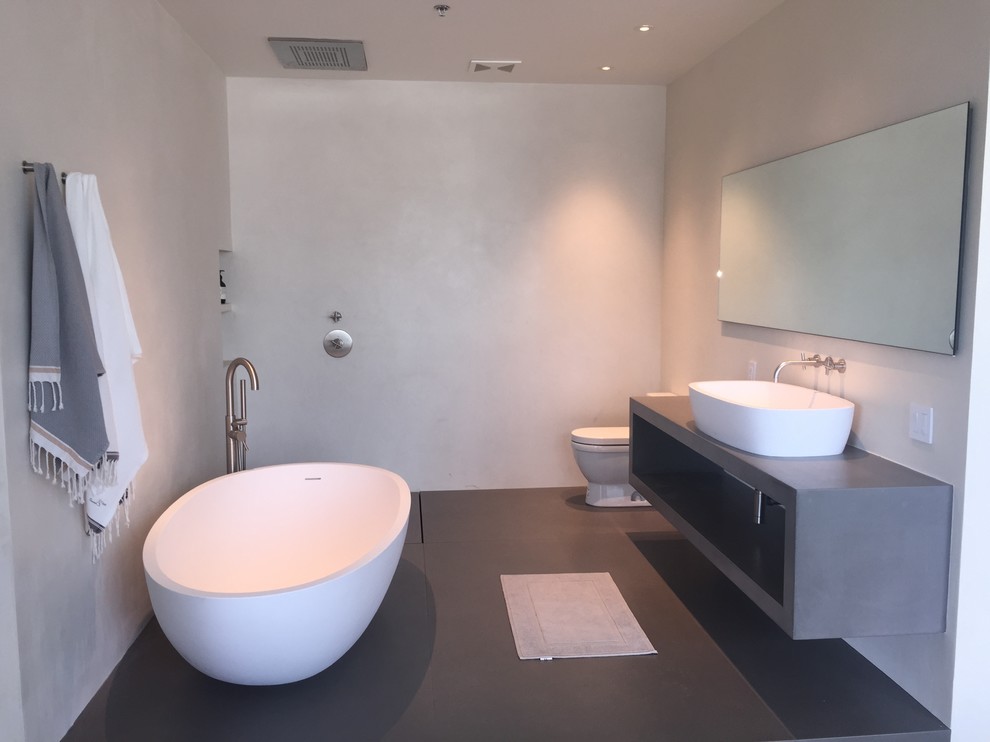 Пример оригинального дизайна: главная ванная комната среднего размера в стиле модернизм с открытыми фасадами, серыми фасадами, отдельно стоящей ванной, открытым душем, унитазом-моноблоком, настольной раковиной, белыми стенами, бетонным полом и столешницей из бетона