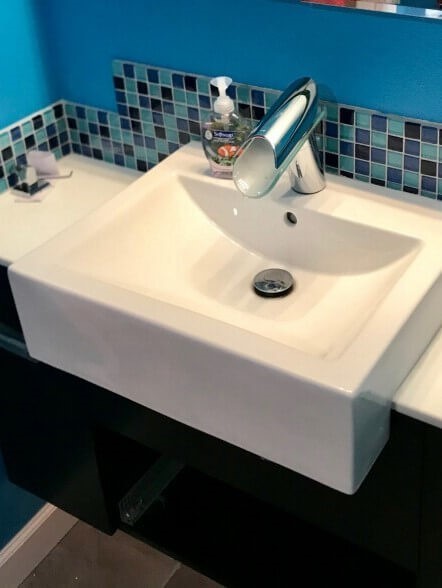 Cette photo montre une salle de bain moderne en bois foncé avec un placard à porte plane, un combiné douche/baignoire, un carrelage bleu, un carrelage en pâte de verre, un mur bleu, un sol en carrelage de porcelaine, une vasque, un plan de toilette en quartz modifié et un sol beige.