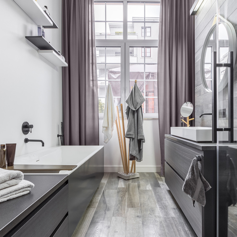 Diseño de cuarto de baño actual con armarios con paneles lisos, puertas de armario grises, bañera exenta, paredes blancas, aseo y ducha, lavabo sobreencimera, suelo gris y encimeras grises