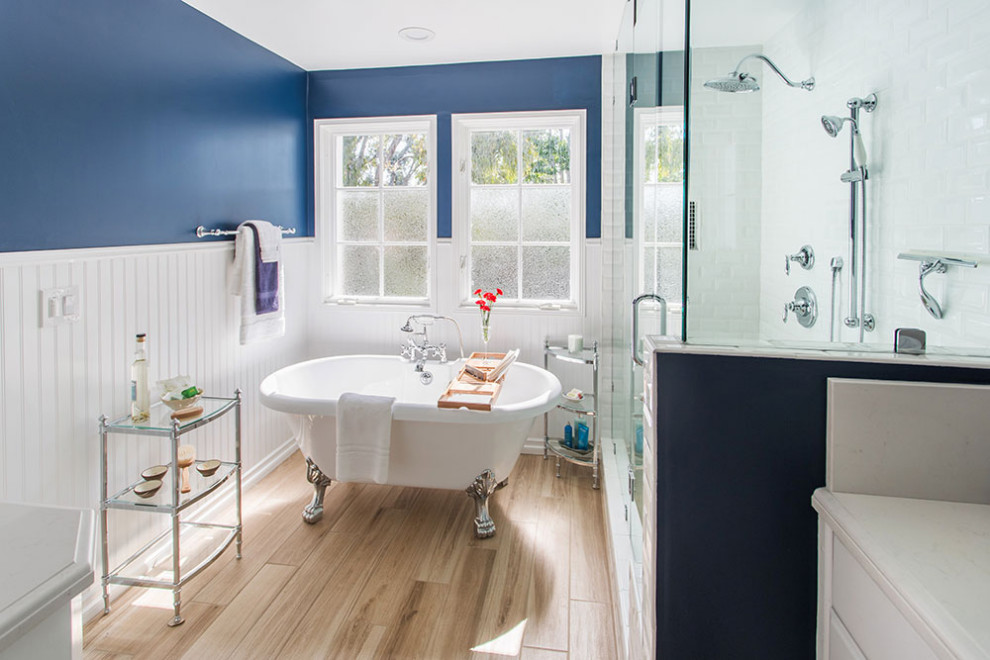 Large modern ensuite wet room bathroom in Los Angeles with flat-panel cabinets, white cabinets, a claw-foot bath, blue tiles, blue walls, laminate floors, a vessel sink, granite worktops, brown floors, a hinged door and white worktops.