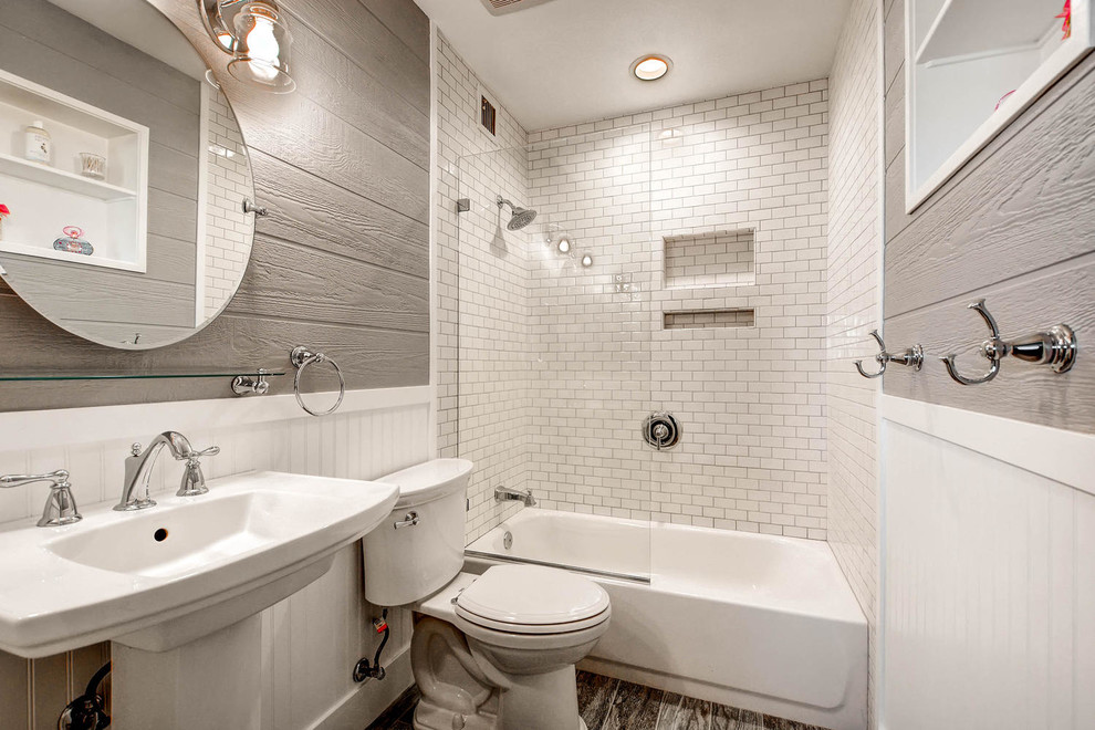 Foto på ett litet funkis badrum, med ett badkar i en alkov, en dusch/badkar-kombination, en toalettstol med hel cisternkåpa, vit kakel, tunnelbanekakel, grå väggar, mellanmörkt trägolv, ett piedestal handfat och bänkskiva i akrylsten