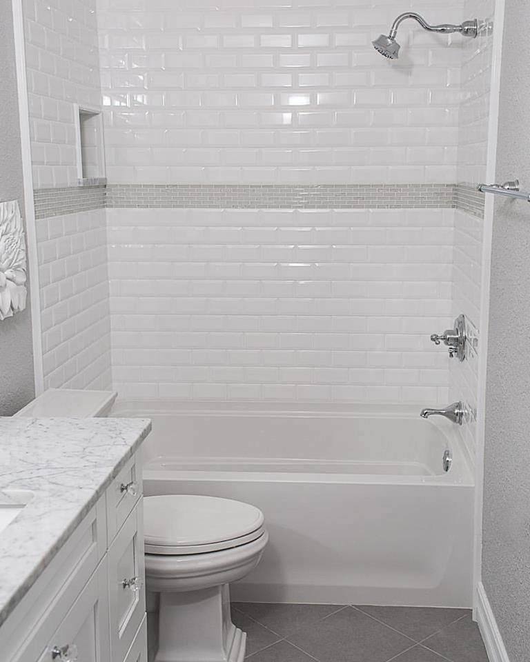 Cette photo montre une salle de bain moderne de taille moyenne avec un placard à porte shaker, des portes de placard blanches, une baignoire en alcôve, un combiné douche/baignoire, WC à poser, un carrelage blanc, un carrelage métro, un mur gris, un lavabo encastré, un plan de toilette en marbre, un sol gris et une cabine de douche avec un rideau.
