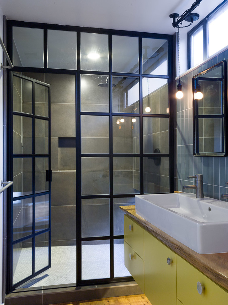Modelo de cuarto de baño urbano con lavabo sobreencimera, encimera de madera, puertas de armario amarillas y encimeras marrones