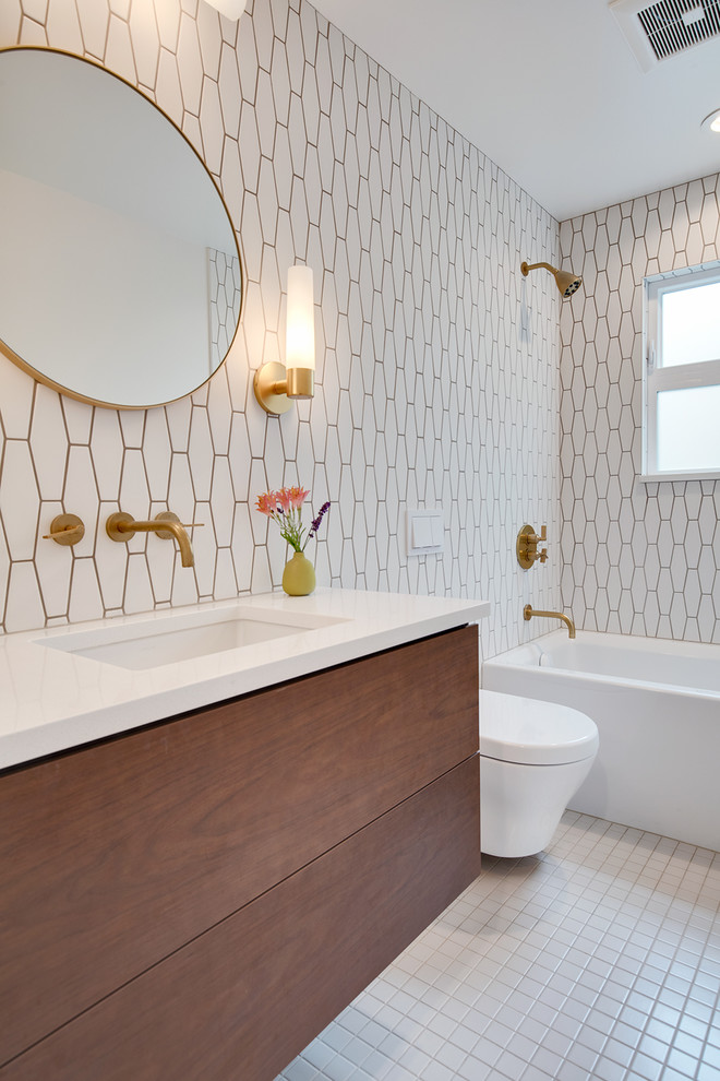 シアトルにある高級な中くらいなコンテンポラリースタイルのおしゃれな浴室 (フラットパネル扉のキャビネット、中間色木目調キャビネット、シャワー付き浴槽	、一体型トイレ	、白いタイル、セメントタイル、白い壁、セラミックタイルの床、オーバーカウンターシンク、珪岩の洗面台、白い床、白い洗面カウンター、アルコーブ型浴槽) の写真