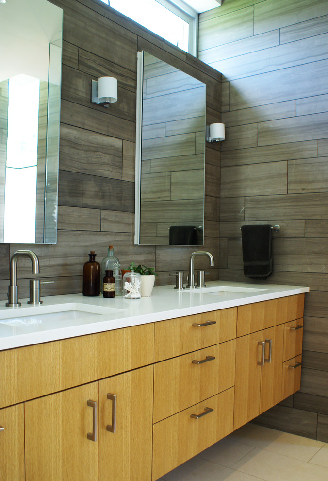 Diseño de cuarto de baño minimalista con lavabo bajoencimera, armarios con paneles lisos, baldosas y/o azulejos grises y puertas de armario de madera clara