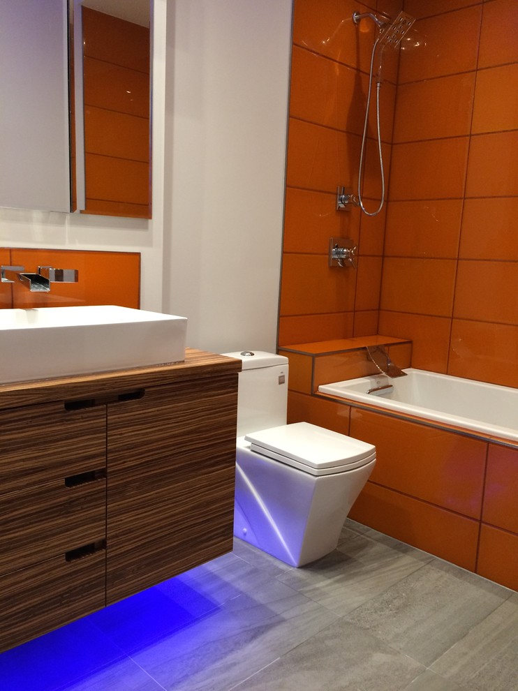 Свежая идея для дизайна: ванная комната в стиле модернизм с плоскими фасадами, фасадами цвета дерева среднего тона, ванной в нише, душем над ванной, оранжевой плиткой, керамогранитной плиткой, белыми стенами, полом из керамической плитки и настольной раковиной - отличное фото интерьера
