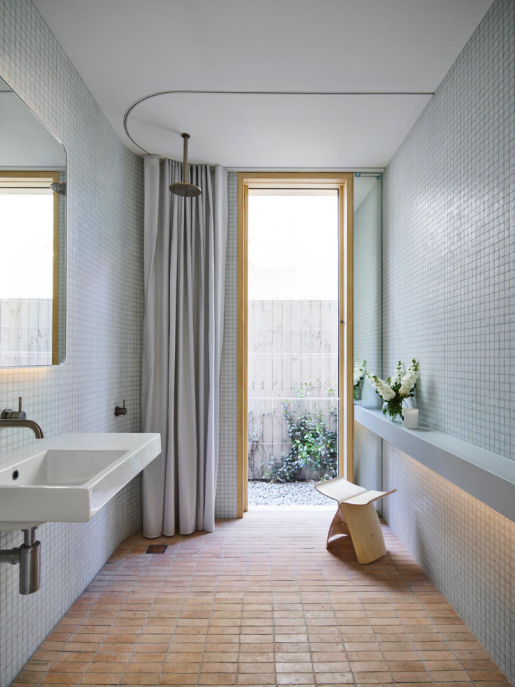 Immagine di una stanza da bagno minimalista con doccia a filo pavimento, piastrelle grigie, piastrelle a mosaico, pavimento in mattoni, lavabo sospeso, pavimento marrone, doccia con tenda e un lavabo