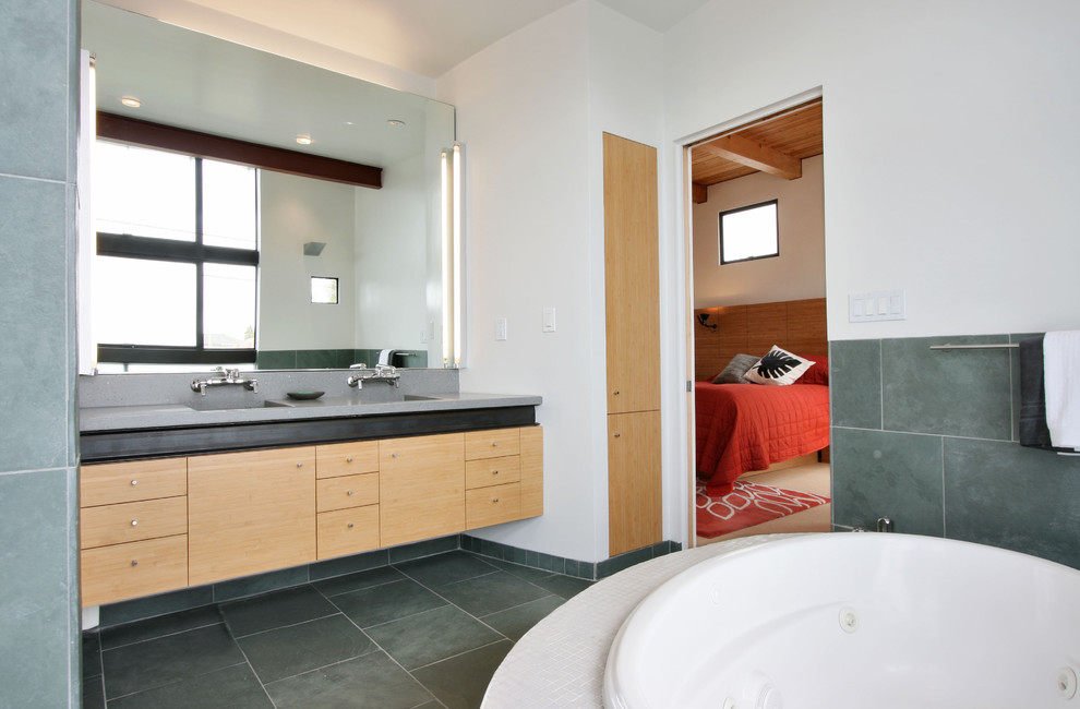 Photo of a modern bathroom in San Francisco with an integrated sink, flat-panel cabinets, light wood cabinets, a built-in bath, green tiles, black floors and grey worktops.