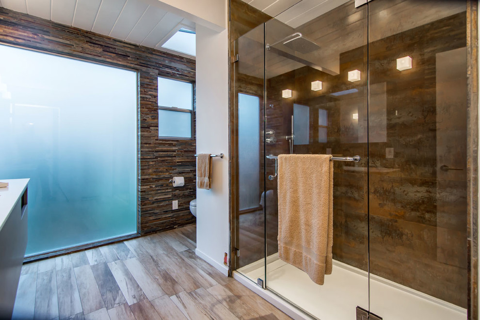 Пример оригинального дизайна: главная ванная комната среднего размера в стиле модернизм с консольной раковиной, коричневыми фасадами, двойным душем, унитазом-моноблоком, коричневой плиткой, керамогранитной плиткой, коричневыми стенами, полом из керамогранита, столешницей из ламината, коричневым полом, душем с распашными дверями и белой столешницей