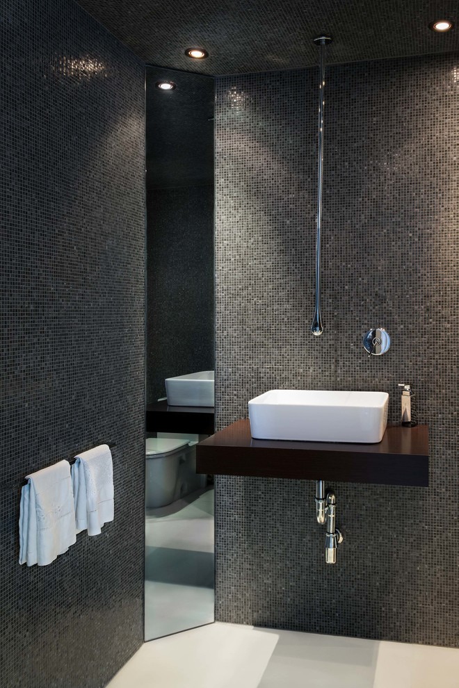 На фото: главная ванная комната среднего размера в стиле модернизм с настольной раковиной, темными деревянными фасадами, столешницей из дерева, раздельным унитазом, серой плиткой, стеклянной плиткой и серыми стенами с