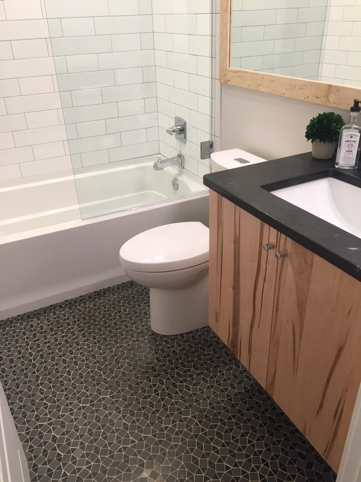 Idéer för att renovera ett litet funkis badrum med dusch, med släta luckor, skåp i ljust trä, en toalettstol med hel cisternkåpa, ett badkar i en alkov, en dusch/badkar-kombination, vit kakel, keramikplattor, grå väggar, ett undermonterad handfat, bänkskiva i täljsten, svart golv och med dusch som är öppen