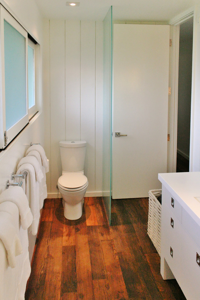 This is an example of a small family bathroom in Hawaii with flat-panel cabinets, white cabinets, an alcove shower, a one-piece toilet, white walls, dark hardwood flooring, solid surface worktops, brown floors and an open shower.