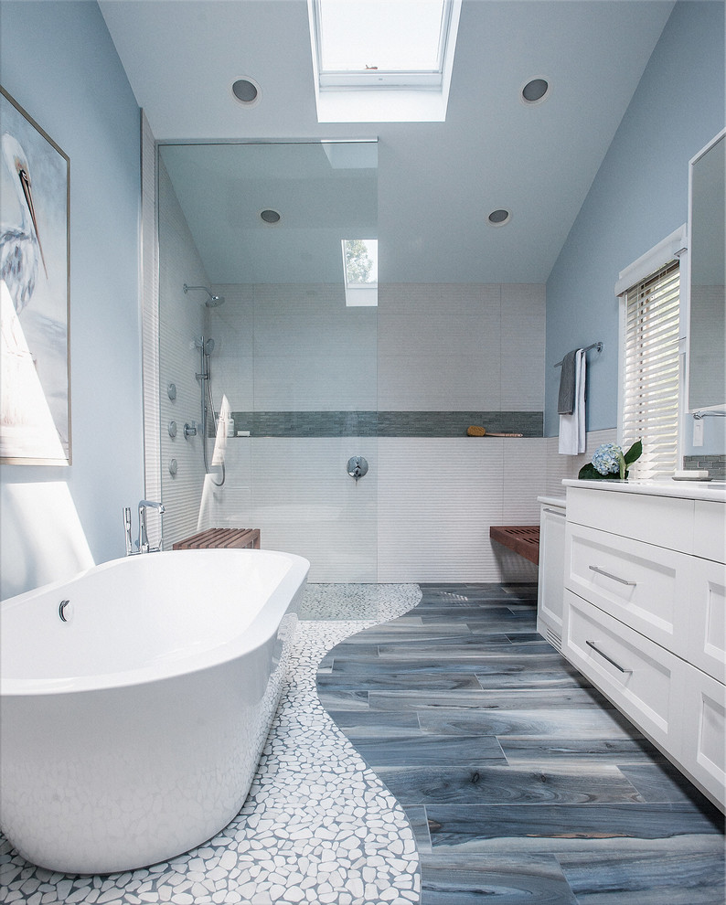 На фото: большая главная ванная комната в стиле модернизм с фасадами в стиле шейкер, белыми фасадами, отдельно стоящей ванной, душем без бортиков, раздельным унитазом, бежевой плиткой, керамогранитной плиткой, синими стенами, полом из керамогранита, врезной раковиной, столешницей из искусственного кварца, синим полом, открытым душем и белой столешницей с