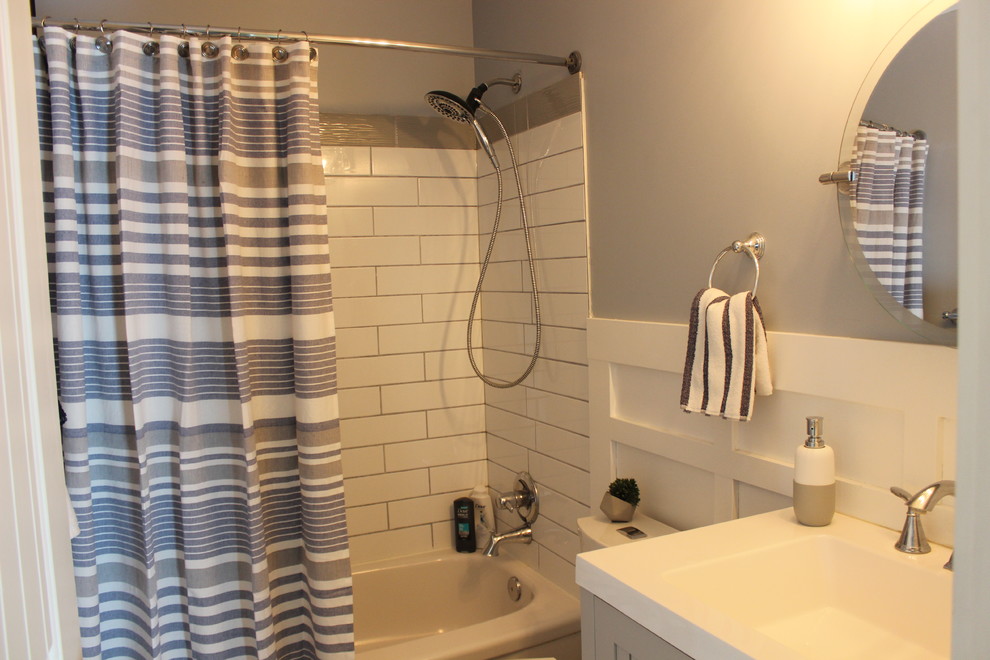 Inspiration for a medium sized nautical ensuite bathroom in Calgary with raised-panel cabinets, grey cabinets, an alcove bath, a shower/bath combination, a two-piece toilet, white tiles, metro tiles, blue walls, porcelain flooring, an integrated sink, solid surface worktops, white floors, a shower curtain and white worktops.