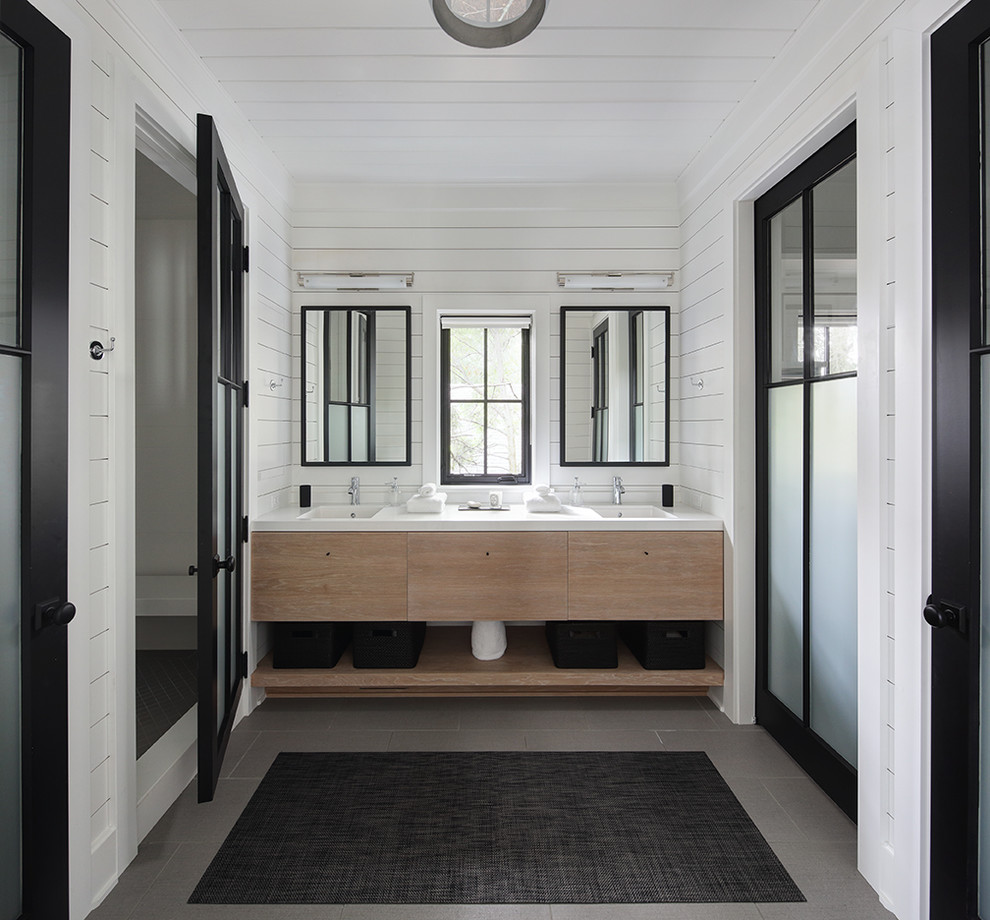 Country gray floor bathroom photo in Milwaukee with flat-panel cabinets, light wood cabinets, white walls, an integrated sink and white countertops