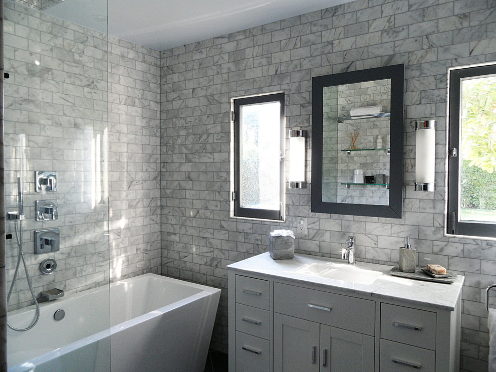 Exemple d'une salle de bain principale moderne avec des portes de placard blanches, un plan de toilette en marbre, une baignoire indépendante, un carrelage de pierre et un sol en carrelage de porcelaine.