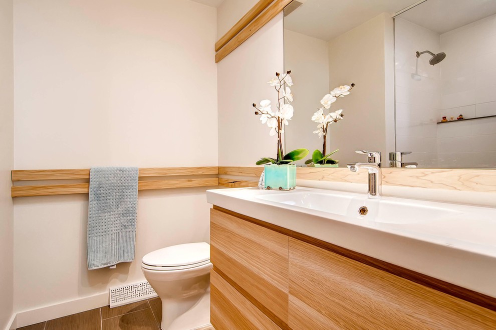 Aménagement d'une salle de bain moderne en bois clair de taille moyenne avec un lavabo intégré, une baignoire posée, WC séparés, un mur blanc, un placard à porte plane, un carrelage blanc, un carrelage métro, un plan de toilette en surface solide, un combiné douche/baignoire et un sol en carrelage de céramique.