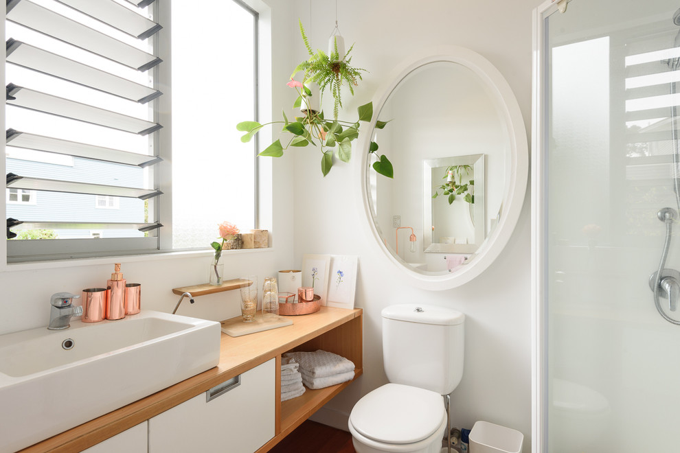 Skandinavisches Badezimmer mit Wandtoilette mit Spülkasten, weißer Wandfarbe, braunem Holzboden und Aufsatzwaschbecken in Auckland