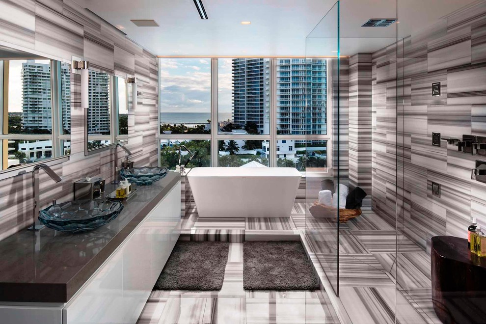 Großes Modernes Badezimmer En Suite mit flächenbündigen Schrankfronten, weißen Schränken, freistehender Badewanne, Eckdusche, grauer Wandfarbe, Marmorboden, Aufsatzwaschbecken und Mineralwerkstoff-Waschtisch in Miami