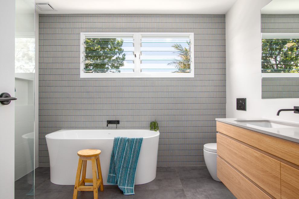 Источник вдохновения для домашнего уюта: детская ванная комната в современном стиле с светлыми деревянными фасадами, отдельно стоящей ванной, синей плиткой, серой плиткой, удлиненной плиткой, белыми стенами, полом из цементной плитки, врезной раковиной, столешницей из искусственного кварца, серым полом, серой столешницей, унитазом-моноблоком и плоскими фасадами