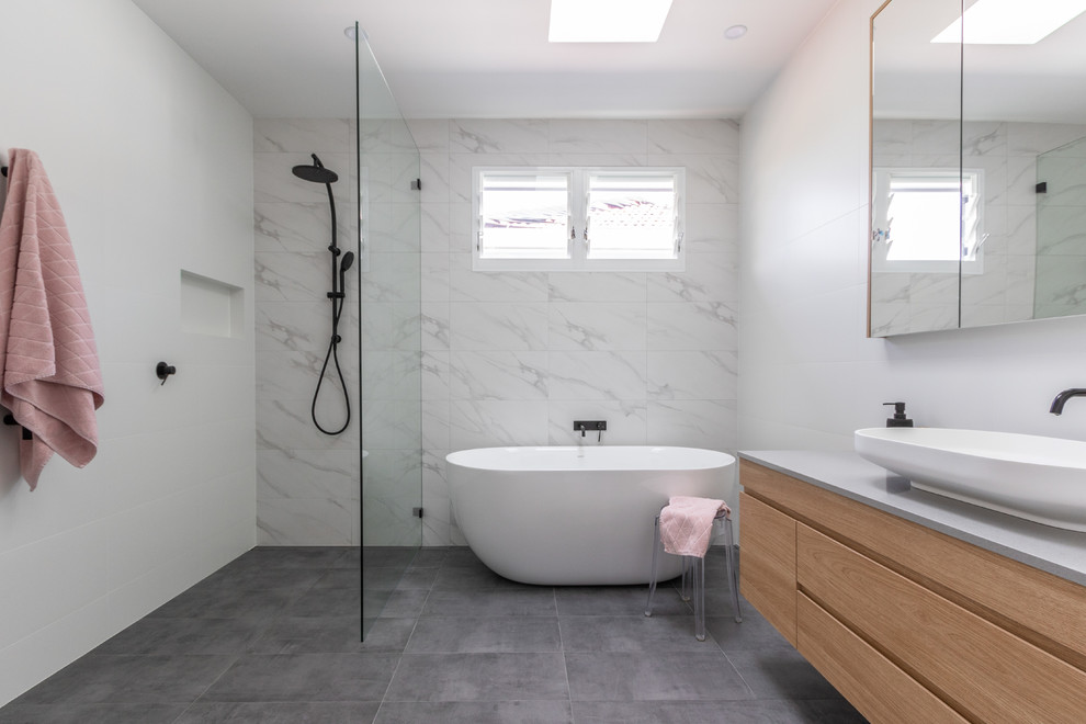 Idéer för att renovera ett funkis grå grått badrum, med skåp i ljust trä, ett fristående badkar, en öppen dusch, vit kakel, keramikplattor, vita väggar, cementgolv, ett fristående handfat, bänkskiva i kvarts, grått golv, med dusch som är öppen och släta luckor