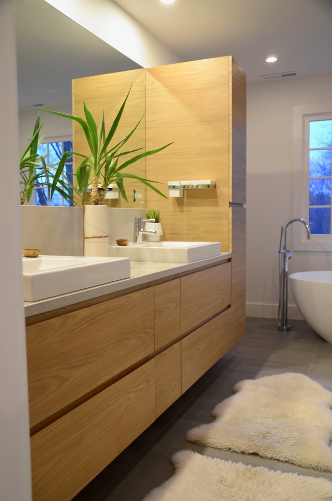 Cette photo montre une grande salle de bain principale moderne en bois clair avec un placard à porte plane, une baignoire indépendante, une douche à l'italienne, un carrelage gris, un carrelage de pierre, un mur blanc, un sol en carrelage de porcelaine, une vasque, un plan de toilette en béton, un sol gris et aucune cabine.