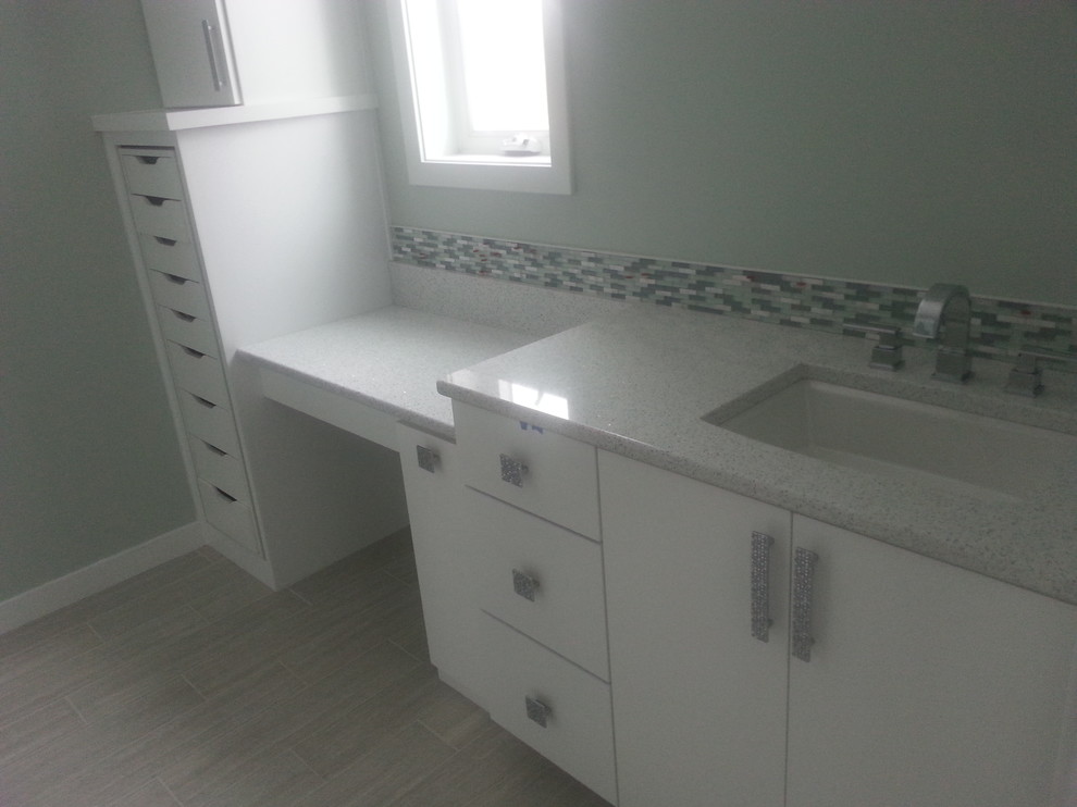 Inredning av ett modernt badrum, med ett undermonterad handfat, släta luckor, vita skåp, bänkskiva i kvartsit, grå kakel, porslinskakel, grå väggar och klinkergolv i porslin