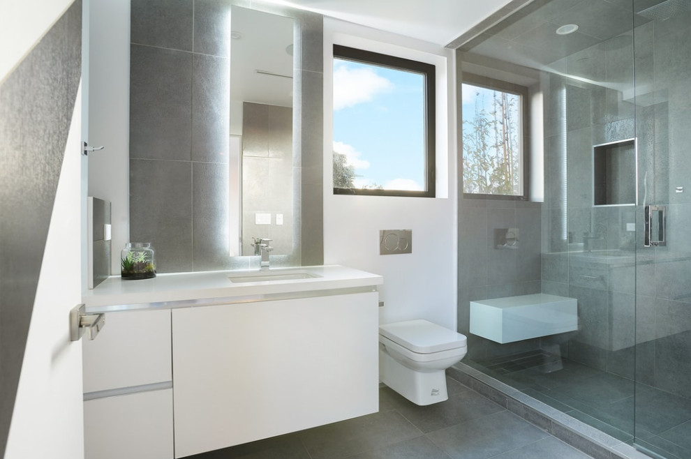 This is an example of a medium sized modern ensuite bathroom in Los Angeles with flat-panel cabinets, white cabinets, a corner shower, a two-piece toilet, grey tiles, ceramic tiles, white walls, ceramic flooring, engineered stone worktops, grey floors, a hinged door, white worktops and a submerged sink.