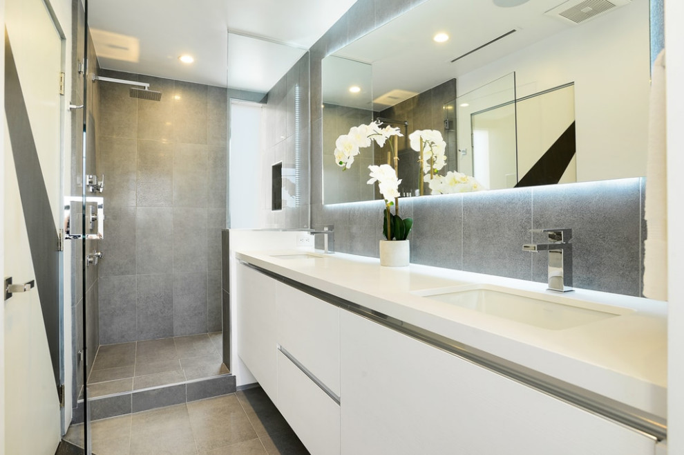 Inspiration for a medium sized modern ensuite bathroom in Los Angeles with flat-panel cabinets, white cabinets, a corner shower, a one-piece toilet, grey tiles, ceramic tiles, white walls, ceramic flooring, a built-in sink, engineered stone worktops, grey floors, a hinged door and white worktops.