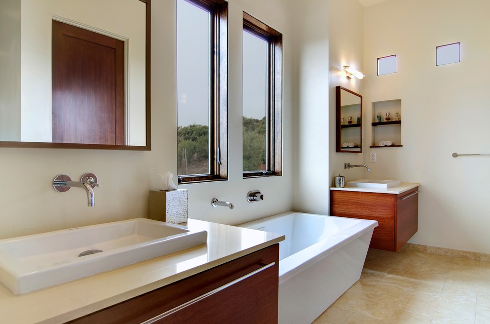 Пример оригинального дизайна: большая ванная комната в средиземноморском стиле с накладной раковиной, плоскими фасадами, фасадами цвета дерева среднего тона, отдельно стоящей ванной, душем в нише, унитазом-моноблоком, белыми стенами, полом из травертина, столешницей из искусственного кварца, бежевым полом, душем с распашными дверями и белой столешницей
