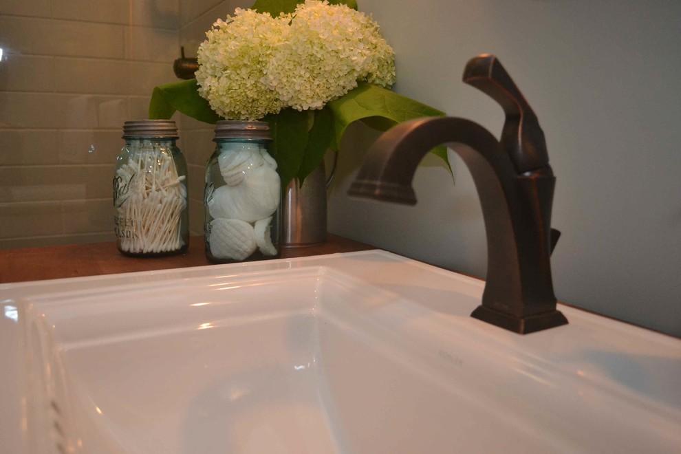 Inredning av ett eklektiskt litet badrum, med öppna hyllor, turkosa skåp, en dusch i en alkov, en toalettstol med separat cisternkåpa, blå väggar, klinkergolv i porslin, ett nedsänkt handfat, träbänkskiva, grått golv och dusch med gångjärnsdörr