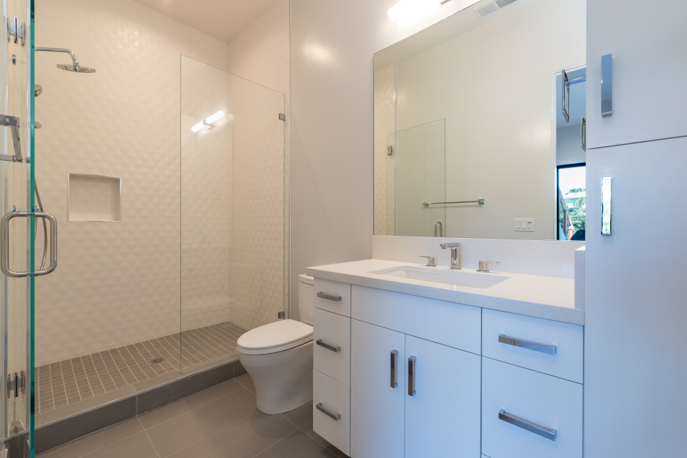 Idéer för stora funkis vitt badrum med dusch, med släta luckor, vita skåp, en dusch i en alkov, en toalettstol med hel cisternkåpa, vit kakel, porslinskakel, grå väggar, klinkergolv i porslin, ett undermonterad handfat, bänkskiva i kvarts, grått golv och dusch med gångjärnsdörr