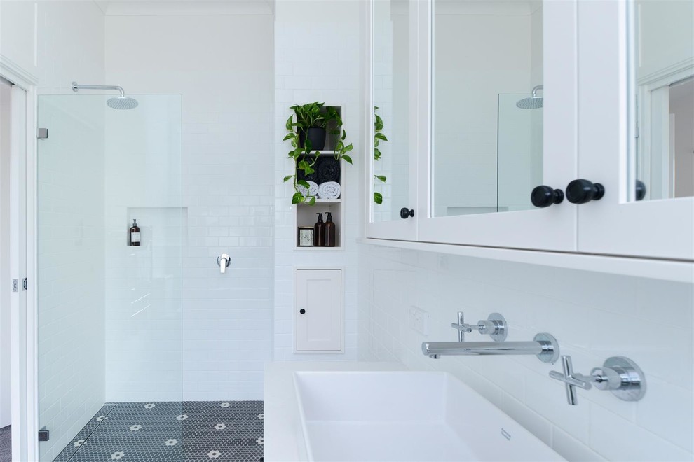 Idéer för att renovera ett mellanstort funkis vit vitt badrum med dusch, med skåp i shakerstil, vita skåp, ett fristående badkar, en dusch i en alkov, en toalettstol med separat cisternkåpa, vit kakel, keramikplattor, vita väggar, mosaikgolv, ett fristående handfat, bänkskiva i akrylsten, flerfärgat golv och med dusch som är öppen