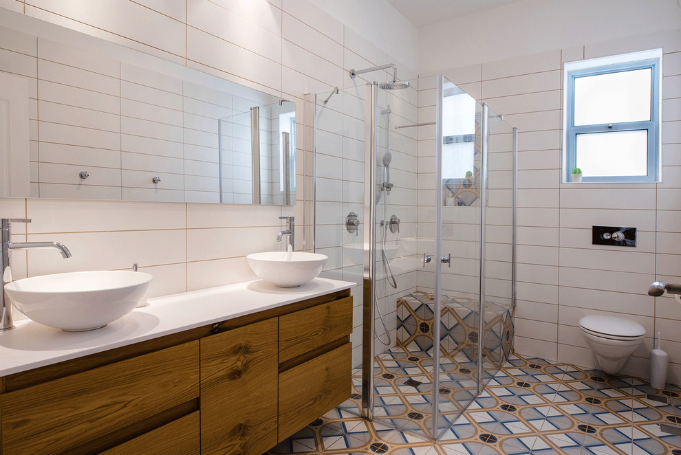На фото: большая главная ванная комната в стиле фьюжн с плоскими фасадами, светлыми деревянными фасадами, угловым душем, инсталляцией, белой плиткой, керамогранитной плиткой, белыми стенами, настольной раковиной, столешницей из искусственного камня, синим полом, душем с распашными дверями, белой столешницей, полом из керамической плитки, сиденьем для душа и подвесной тумбой