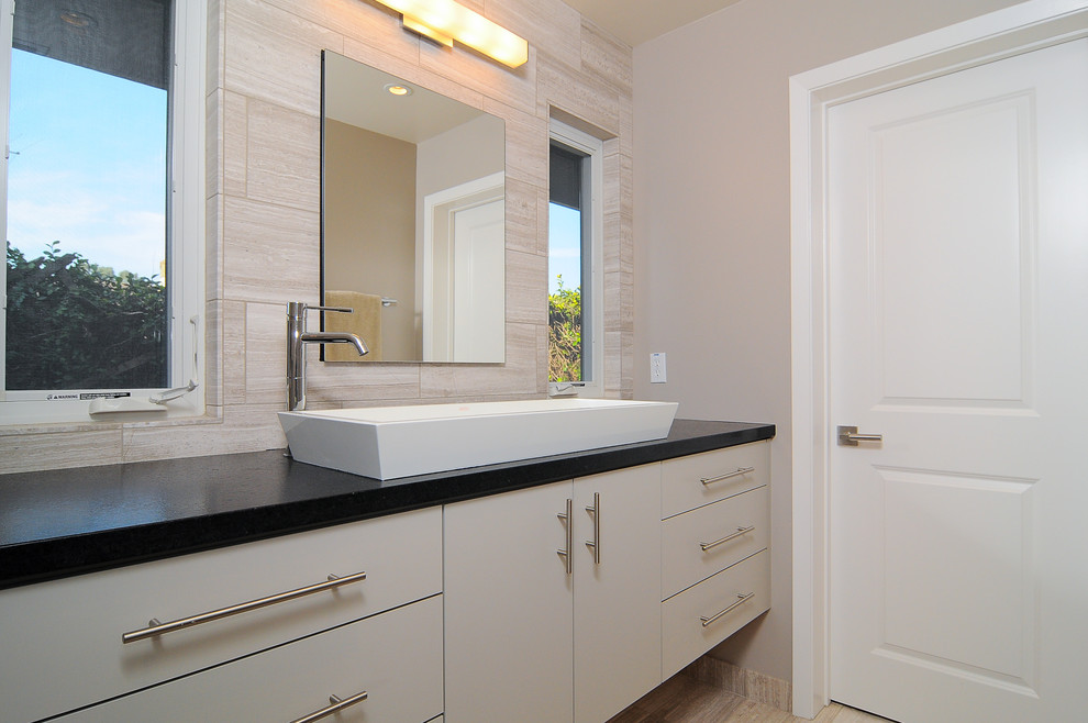 Cette photo montre une salle de bain moderne avec une vasque, un placard à porte plane, des portes de placard blanches et un carrelage beige.