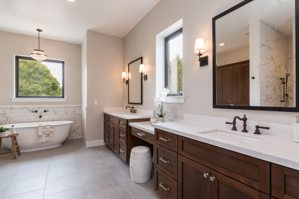 Photo of a medium sized country ensuite bathroom in San Luis Obispo with recessed-panel cabinets, brown cabinets, a freestanding bath, a shower/bath combination, a one-piece toilet, white tiles, ceramic tiles, grey walls, ceramic flooring, a submerged sink, quartz worktops, grey floors, an open shower and white worktops.