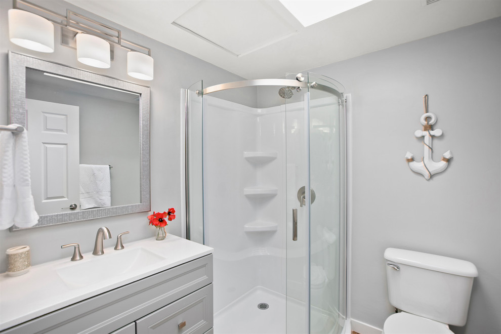 Bild på ett litet maritimt vit vitt badrum med dusch, med skåp i shakerstil, grå skåp, en hörndusch, en toalettstol med separat cisternkåpa, grå väggar, vinylgolv, ett integrerad handfat, bänkskiva i kvartsit, flerfärgat golv och dusch med skjutdörr
