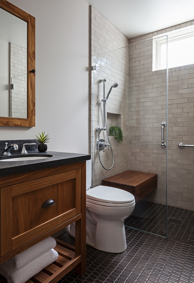 Exempel på ett mellanstort amerikanskt badrum med dusch, med luckor med infälld panel, skåp i mörkt trä, en kantlös dusch, en toalettstol med separat cisternkåpa, beige kakel, tunnelbanekakel, vita väggar, klinkergolv i keramik, ett undermonterad handfat, bänkskiva i täljsten, svart golv och med dusch som är öppen