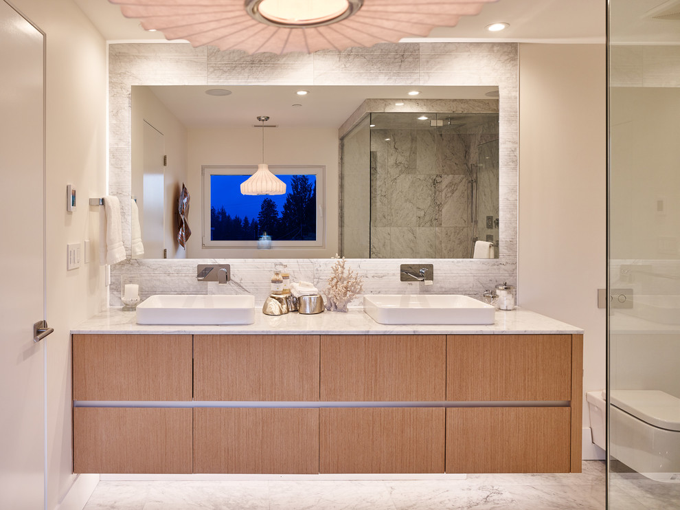 Свежая идея для дизайна: большая главная ванная комната в стиле модернизм с плоскими фасадами, светлыми деревянными фасадами, отдельно стоящей ванной, открытым душем, унитазом-моноблоком, белыми стенами, мраморным полом, настольной раковиной, мраморной столешницей, серым полом, душем с распашными дверями и белой столешницей - отличное фото интерьера