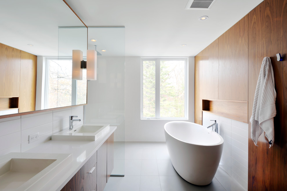 Foto de cuarto de baño moderno con lavabo encastrado, armarios con paneles lisos, puertas de armario de madera oscura, bañera exenta y baldosas y/o azulejos grises