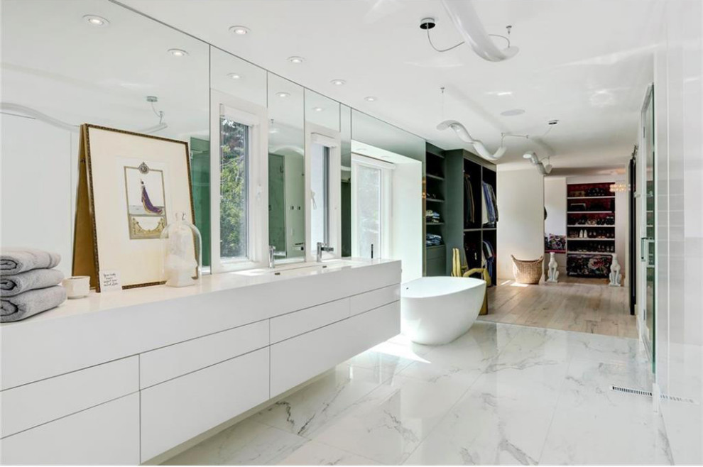 Ispirazione per una stanza da bagno padronale design con ante lisce, ante bianche, vasca freestanding, piastrelle a specchio, pavimento in marmo, lavabo rettangolare, pavimento bianco e top bianco
